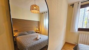 Ein Schlafzimmer mit Bett, Nachttisch, Lampe und einem Fenster mit Vorhängen.