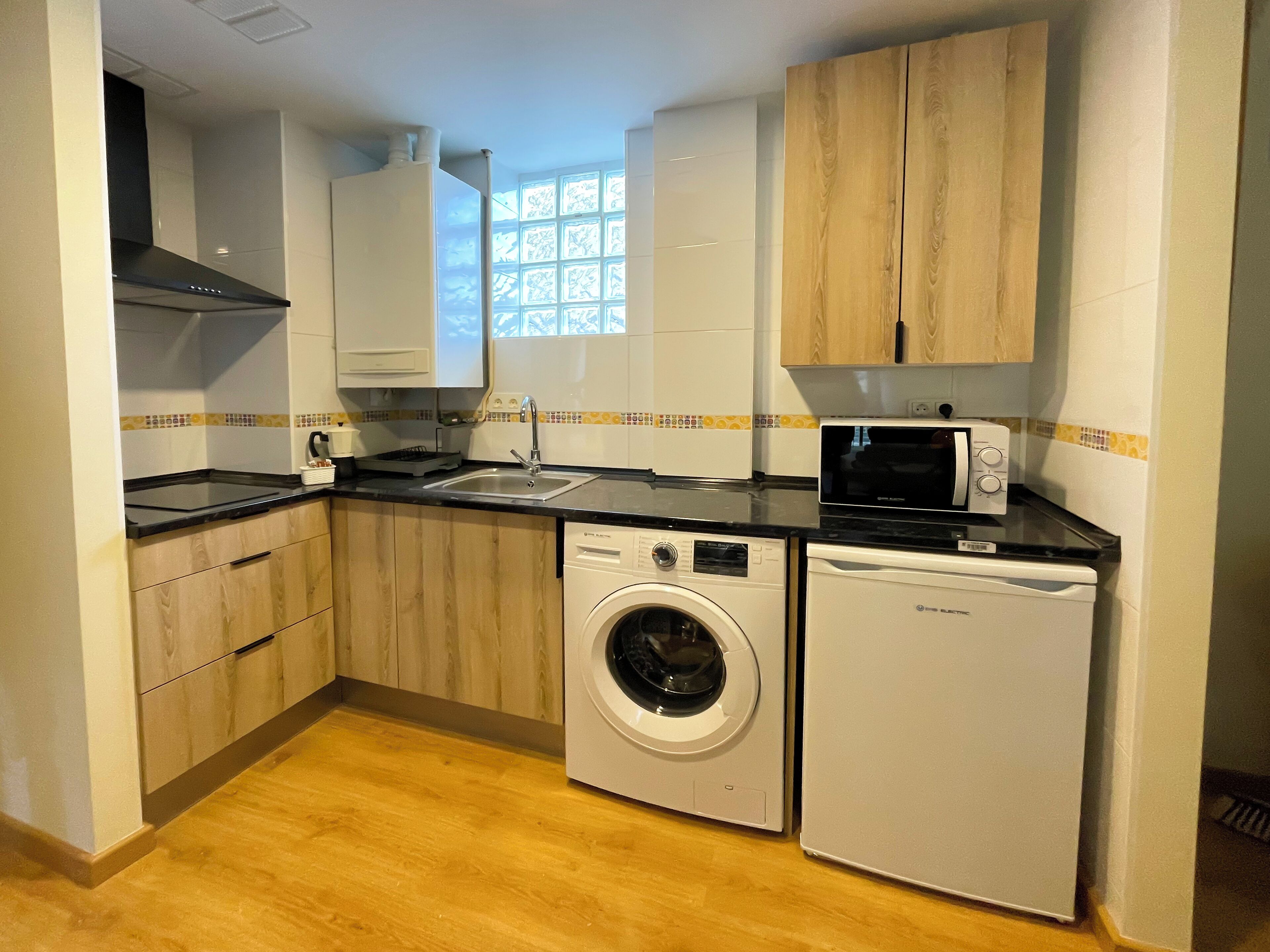 A compact kitchen with a microwave, sink, washing machine, and wooden cabinets.