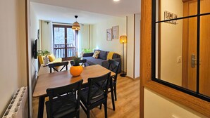 Ein modernes Wohnzimmer mit Essbereich, einer Couch, einem Couchtisch und einem Fernseher.