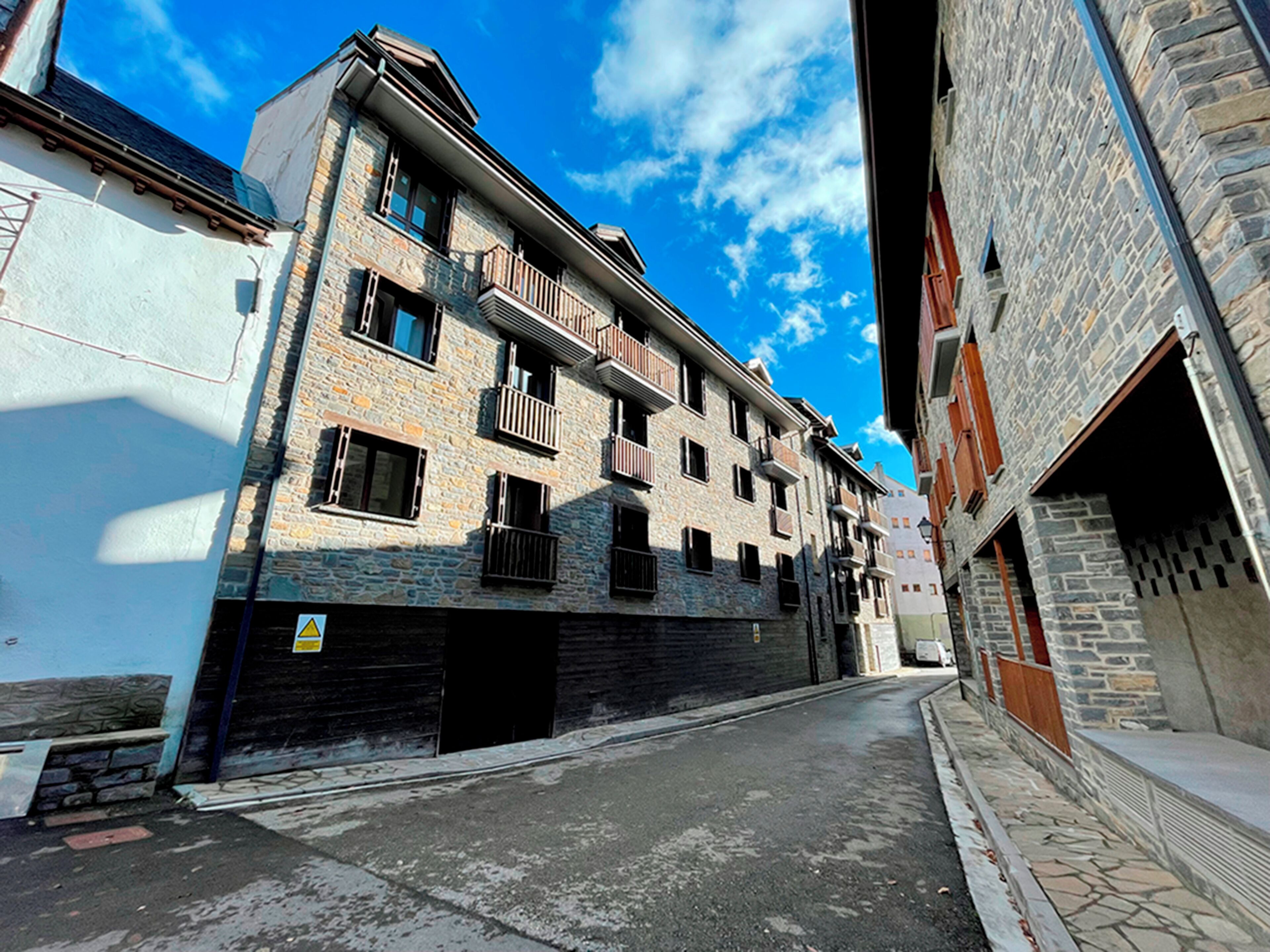 A narrow street with a building featuring stone facade and multiple balconies.
