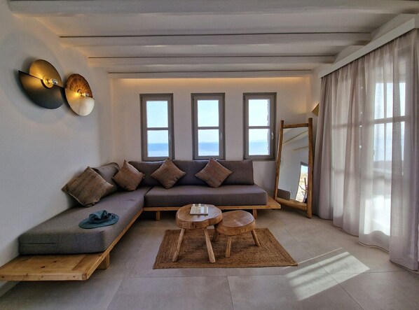 A modern living room with a sofa, two side tables, and a view of the sea through large windows.