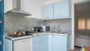 Cocina compacta con microondas, hervidor y frutero. Hay un lavabo y una estufa. Los armarios son de azul claro y el salpicadero es de mármol.
