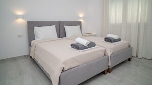 Una cama doble con cabecera gris, dos mesitas de noche y una ventana con cortinas traslúcidas.