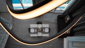 Una habitación de hotel moderna con una mesa de comedor para dos personas, una escalera y vistas a la piscina.
