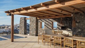 Une terrasse extérieure avec un mur en pierre, une pergola en bois et un espace repas comprenant des chaises et une table en osier.