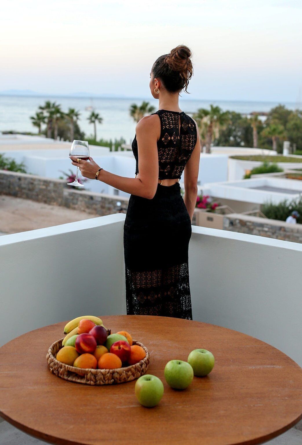 A person standing on a balcony with a table of fruit and a glass of wine.