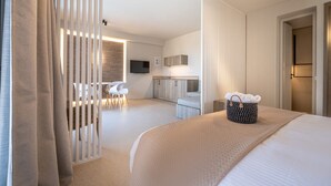 Moderni hotellihuone, jossa on suuri sänky, työpöytä, tuoli, televisio ja pieni keittiönurkkaus.