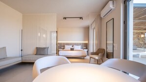 Moderni hotellihuone, jossa on sänky, oleskelualue sohvineen ja tuoleineen sekä suuri ikkuna, josta avautuu näkymä ulos.