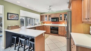 Una cucina moderna con isola centrale, pensili in legno, frigorifero in acciaio inossidabile e ventilatore a soffitto.