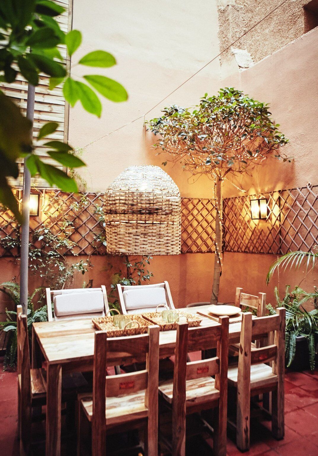 An outdoor dining area with wooden tables and chairs, a woven basket, and a tree.