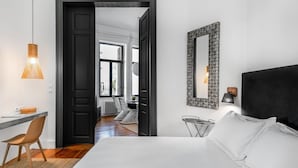 Une chambre d’hôtel avec un lit, un bureau et une chaise. Une porte donne accès à une autre pièce.
