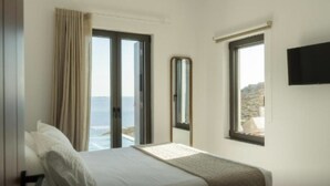 Een hotelkamer met een bed, een groot raam met uitzicht op zee, een spiegel en een wandgemonteerde flatscreen-televisie.