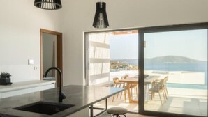 Een moderne keuken met een groot schiereiland, een eethoek met buitenplaatsen, en uitzicht op zee.
