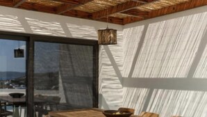 Een moderne eetruimte met een houten tafel en stoelen, een hanglamp en uitzicht door een glazen deur.