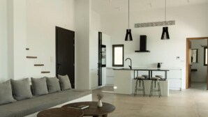 Een moderne woonkamer met een bank, twee salontafels en een keukenhoek met een spoelbak en barkrukken.