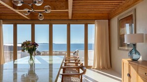 Une pièce spacieuse avec une grande table en verre, des chaises en bois, un vase rempli de fleurs, un meuble en bois et une vue sur la mer.