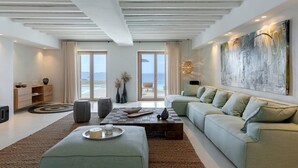 Un salon moderne avec un grand canapé, une table basse et une vue sur l’océan grâce à de grandes fenêtres.