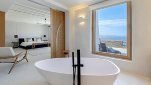 Une salle de bain moderne avec une grande baignoire, un plancher en bois et une vue sur la mer, visible à travers une grande fenêtre.