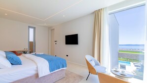 Een moderne hotelkamer met een groot bed, een aan de muur bevestigde televisie, een balkon met uitzicht en een klein tafeltje met een kop.