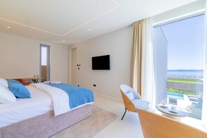 Ein modernes Hotelzimmer mit einem großen Bett, einem an der Wand befestigten Fernseher, einem Balkon mit Blick und einem kleinen Tisch mit einer Tasse.