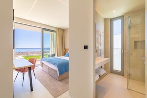 A hotel room with a bed, a desk, a chair, a bathroom with a shower, and a large window with a view of the city. - Villa Azurea Vista | Trogir-Split | Infinity Pool | Sea Views | Luxury Coastal. (Kastel Stari)