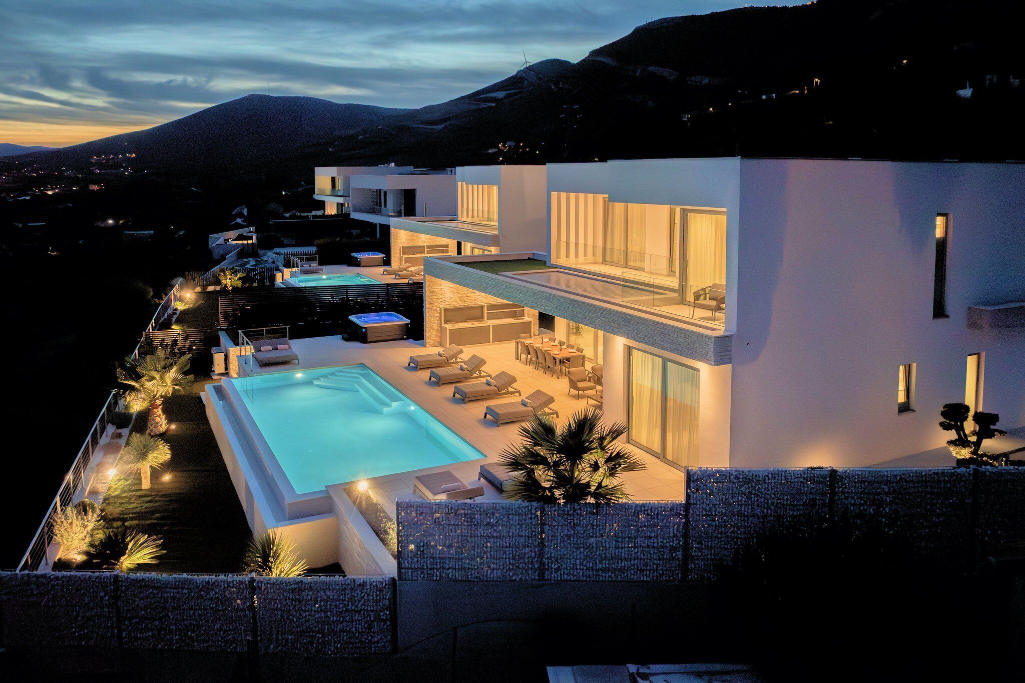 A modern multi-story house with a swimming pool, outdoor seating, and a mountain backdrop.