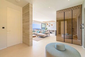 Ein modernes Wohnzimmer mit einer großen Eckcouch, einem runden Couchtisch und einer Glastrennwand mit Blick ins Freie.