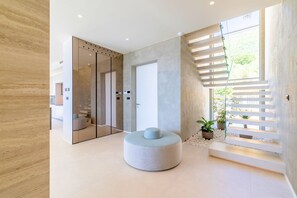 A modern interior with a round seating area, a glass elevator, and a staircase with a view. - Villa Azurea Vista | Trogir-Split | Infinity Pool | Sea Views | Luxury Coastal. (Kastel Stari)
