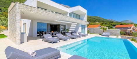 Une maison moderne dotée d’une piscine, d’un espace salon extérieur et offrant une vue sur les montagnes.