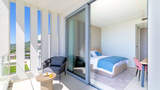 Een moderne hotelkamer met een balkon, een bed, een bureau en een stoel.