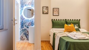 A bedroom with a bed, green bedding, a yellow pillow, and a green headboard. There is a wall with two framed pictures and a door leading to another room. - Pina Colada- New apartment in the historic center of Siena (Siena)