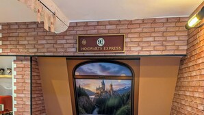 A themed seating area with a Hogwarts Express sign, a window with a scenic view, and a table with a coaster. - The Sorcerer's Den (Caumont-sur-Durance)