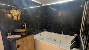 A modern bathroom with a marble wall, a freestanding bathtub, a vanity with a sink, and a decorative mirror. - The Sorcerer's Den (Caumont-sur-Durance)