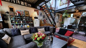 A modern living room with a sofa set, a coffee table with a vase of flowers, and a bookshelf filled with books.