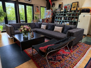 A modern living room with a sectional sofa, a coffee table, and a bench. There is a bookshelf filled with books and decorative items.