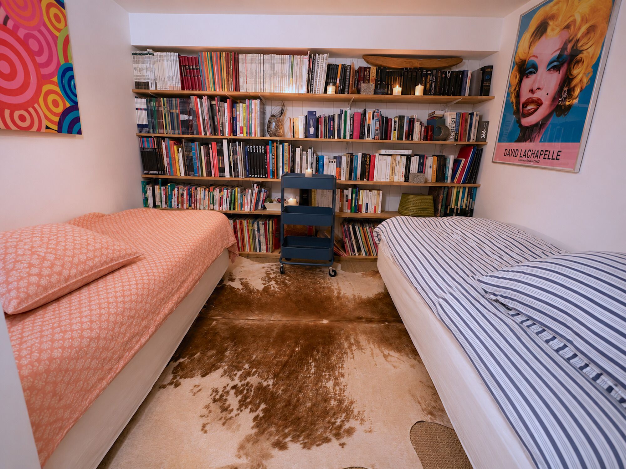 Une chambre avec deux lits, une bibliothèque remplie de livres et une affiche accrochée au mur.