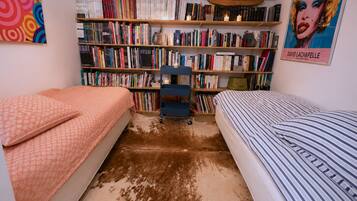 Une chambre avec deux lits, une bibliothèque remplie de livres et une affiche accrochée au mur.