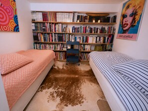 A room with two beds, a bookshelf filled with books, and a poster on the wall.