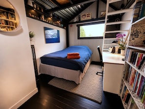A bedroom with a bed, a desk, a bookshelf, and a window.