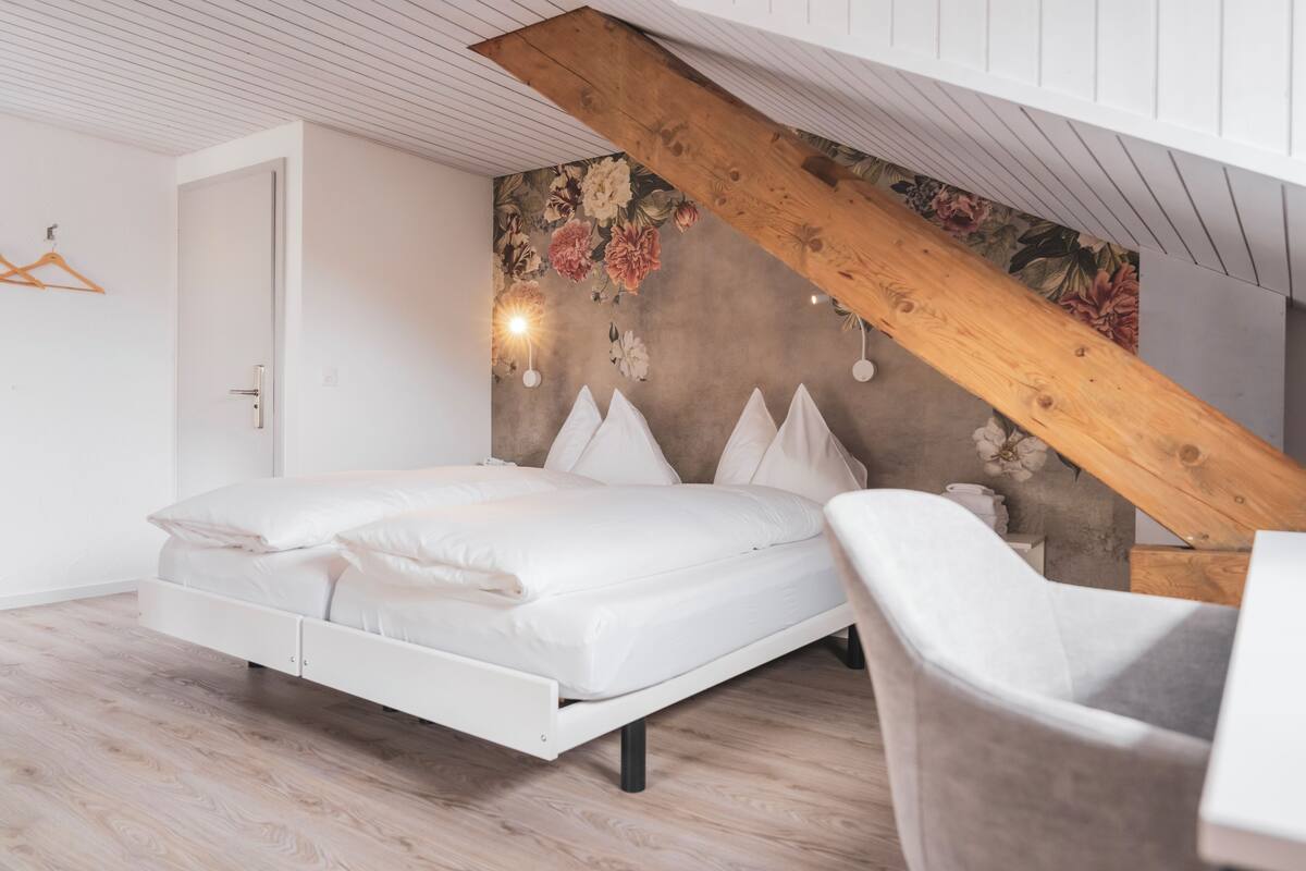 Ein Schlafzimmer mit einer Schlafkoje, Holzbalken, einer Wandmalerei mit Blumenmuster und einem weißen Stuhl.