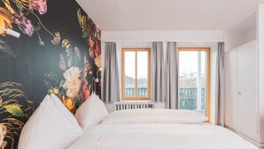 A bedroom with a bed, a radiator, a window with curtains, and a balcony with a railing.