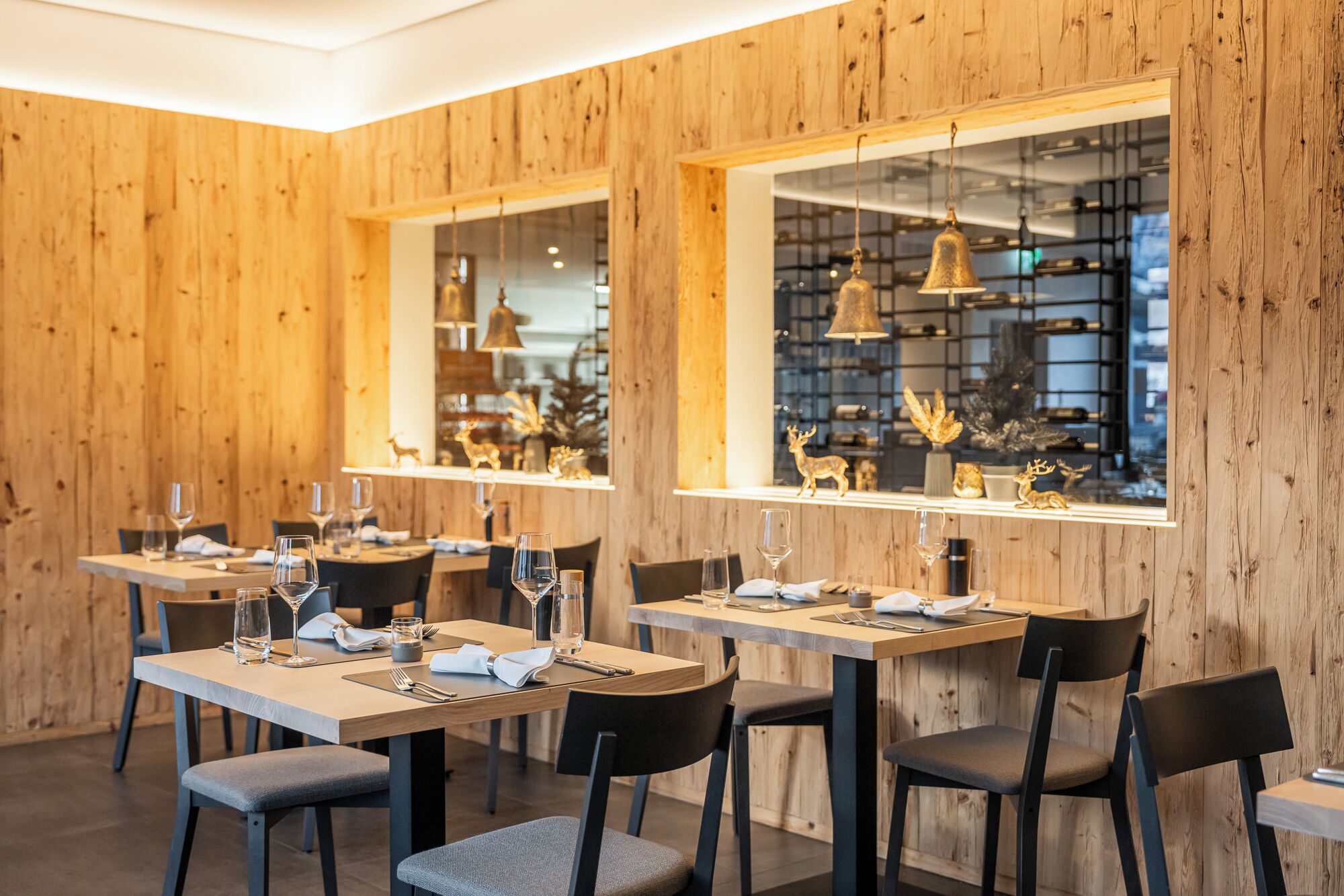A restaurant interior with wooden panel walls, multiple dining tables, chairs, and hanging pendant lights.