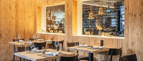 A restaurant interior with wooden panel walls, multiple dining tables, chairs, and hanging pendant lights.