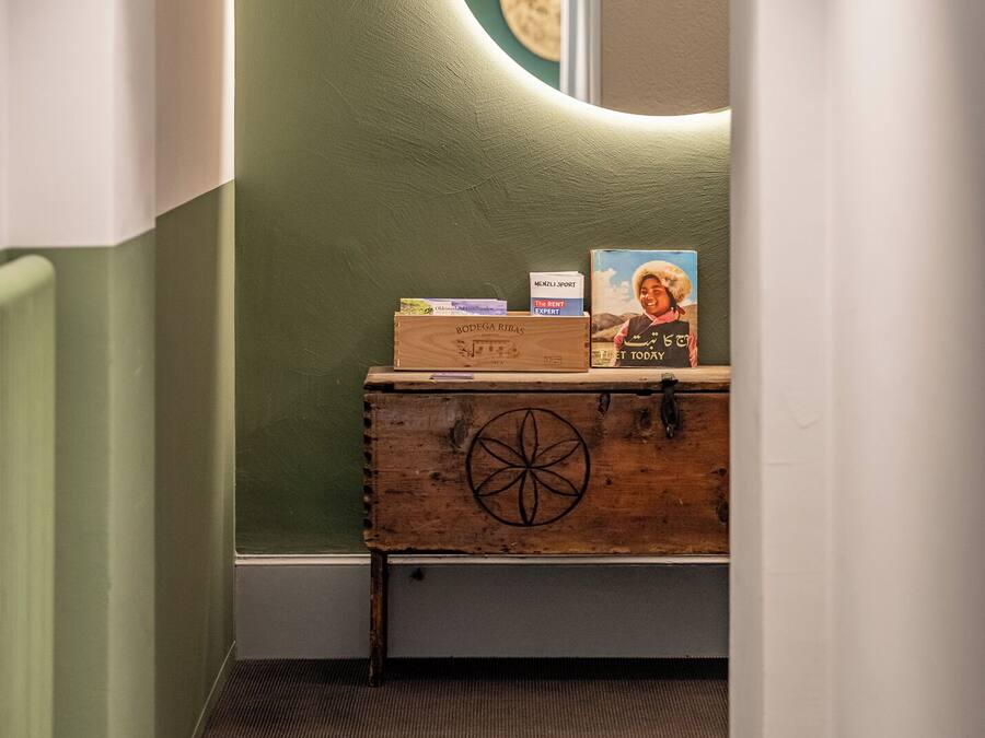A hallway with a wooden chest of drawers, a round mirror, and a green wall.