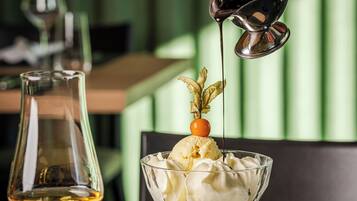 Postre con helado y una cereza en un plato, una copa de vino y una mano sirviendo jarabe.