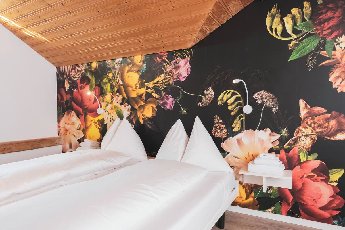 Ein Schlafzimmer mit Holzboden, einem Bett mit weißer Bettwäsche und einer Wand mit floralem Wandbild.