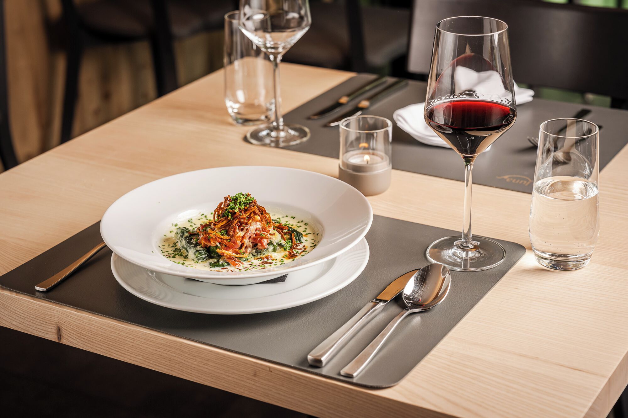 Une table à manger avec une assiette blanche remplie de nourriture, un verre de vin rouge et un verre d  ’eau.