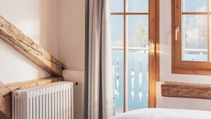 A bedroom with a wooden ceiling, a large window with arched design, a radiator, and a bed.