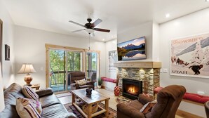 A living room with a fireplace, a ceiling fan, a sofa, a coffee table, and a large window. - Peak Location Near Slopes & Olympic Park (Park City)