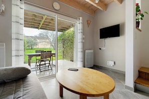 A living room with a sofa, a wooden table, a TV mounted on the wall, and a sliding glass door leading to an outdoor patio.